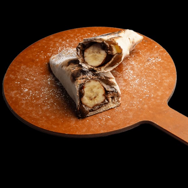 Two halves of a Lebanese flatbread dessert with banana and chocolate on a wooden peel.