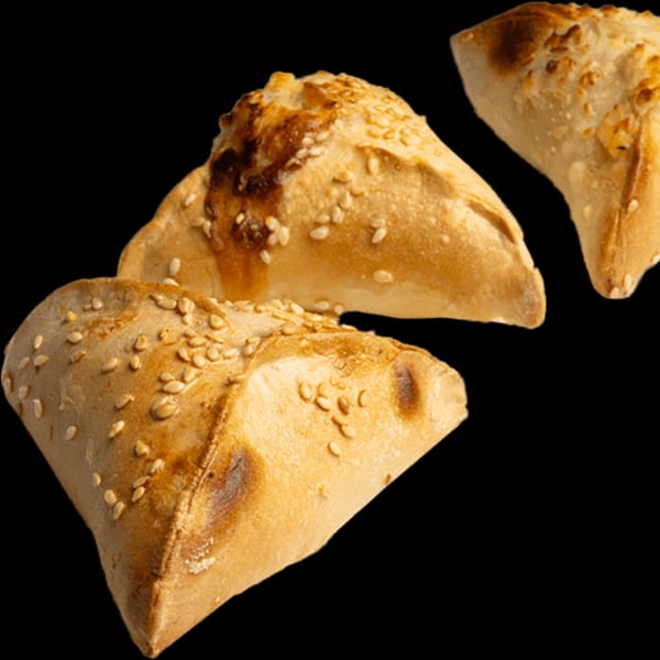Three golden-brown Lebanese flatbreads, triangular in shape, topped with sesame seeds on a black background.