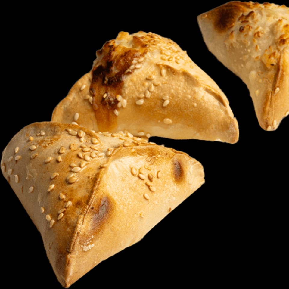 Three golden-brown Lebanese flatbreads, triangular in shape, topped with sesame seeds on a black background.