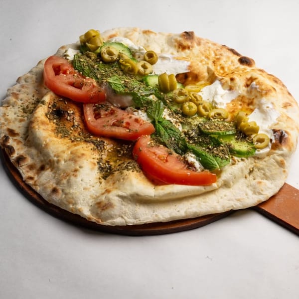 A Lebanese flatbread topped with tomatoes, cucumbers, olives, mint, za'atar, and labneh.
